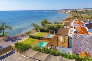 A coastal property with a swimming pool, a tennis court, and a view of the sea.