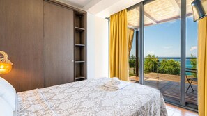 A bedroom with a bed, a wardrobe, and a balcony with a view of the sea. - Kalma Villa Ena in Moudania (Nea Propontida)