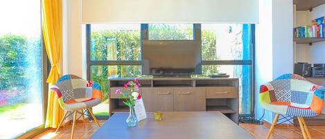 A modern living room with a large TV, two colorful chairs, a coffee table, and a bookshelf.