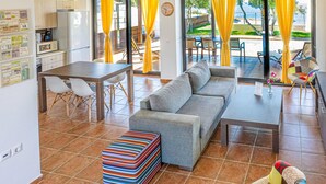 A modern living room with a sofa, a dining table, and a colorful ottoman. - Kalma Villa Ena in Moudania (Nea Propontida)