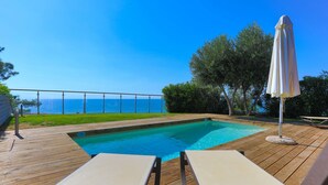 A wooden deck with a swimming pool, lounge chairs, and an umbrella. - Kalma Villa Ena in Moudania (Nea Propontida)