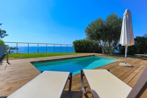 A wooden deck with a swimming pool, lounge chairs, and an umbrella.