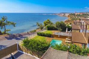 A coastal property with a swimming pool, wooden deck, and a view of the sea.