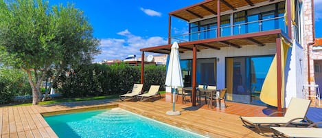 A modern two-story house with a swimming pool, outdoor furniture, and a wooden deck.