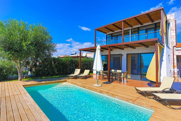 A modern two-story house with a swimming pool, outdoor furniture, and a wooden deck.