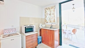 Una cucina compatta con forno a microonde, bollitore e mobiletto. Si vede una finestra con tende floreali e vista sull'esterno.