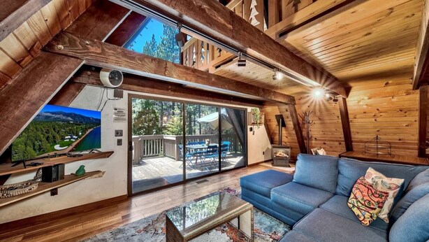 A cozy cabin interior with a large sliding glass door leading to an outdoor deck, a comfortable sofa, and a fireplace. - 3001r Reindeer A Frame Cabin 2 Bedroom Cabin by RedAwning (South Lake Tahoe)