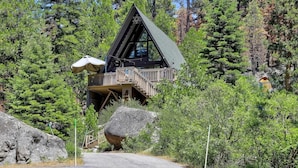 A cabin with a wooden deck, surrounded by dense forest. - 3001r Reindeer A Frame Cabin 2 Bedroom Cabin by RedAwning (South Lake Tahoe)