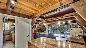 A rustic cabin interior with a kitchen, dining area, and a balcony with a view of the outdoors. - 3001r Reindeer A Frame Cabin 2 Bedroom Cabin by RedAwning (South Lake Tahoe)