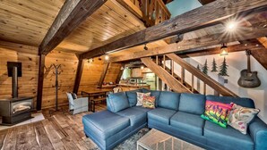 A cozy loft-style room with a blue sectional sofa, a fireplace, wooden beams, and a staircase. - 3001r Reindeer A Frame Cabin 2 Bedroom Cabin by RedAwning (South Lake Tahoe)