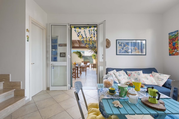 A cozy living room with a blue sofa, a coffee table with various items, and a view into the dining area.