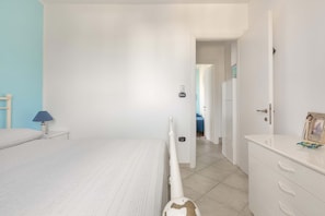 Une chambre à coucher comprenant un lit, une table de chevet avec une lampe, une commode et une porte donnant sur une autre pièce.