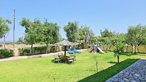 A grassy outdoor area with a small table and chairs, a thatched-roof structure, and a slide. - Amarylis Apartment in Corfu (Corfu)