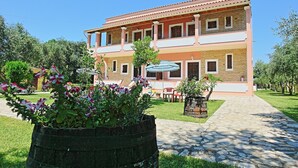 A two-story building with a balcony, a paved courtyard, and potted plants. - Amarylis Apartment in Corfu (Corfu)