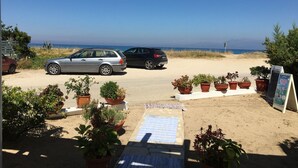 A beachside parking area with two cars, potted plants, and a signboard. - Amarylis Apartment in Corfu (Corfu)