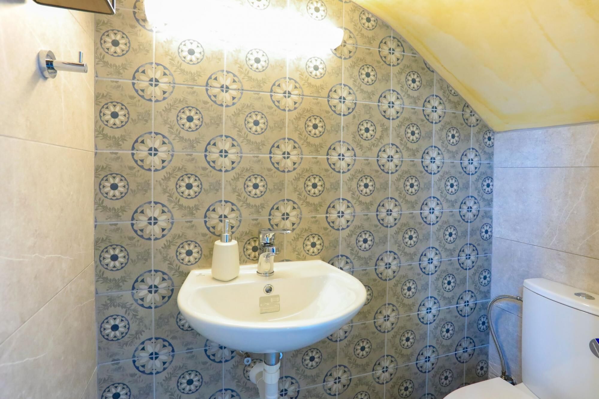 Un baño con un lavamanos blanco, un inodoro y baldosas con diseños en las paredes.