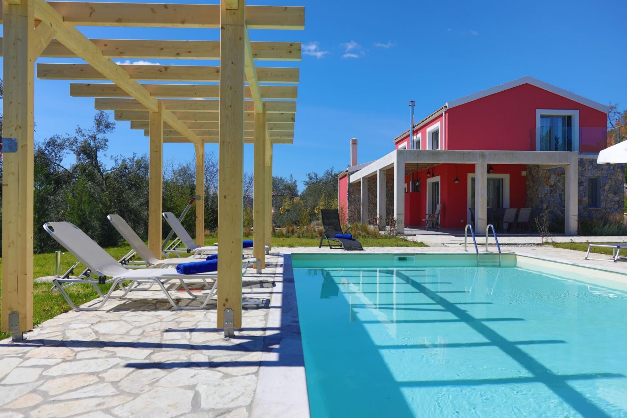 Una piscina con sillones de descanso, una pérgola y un edificio rojo con fachada de piedra.