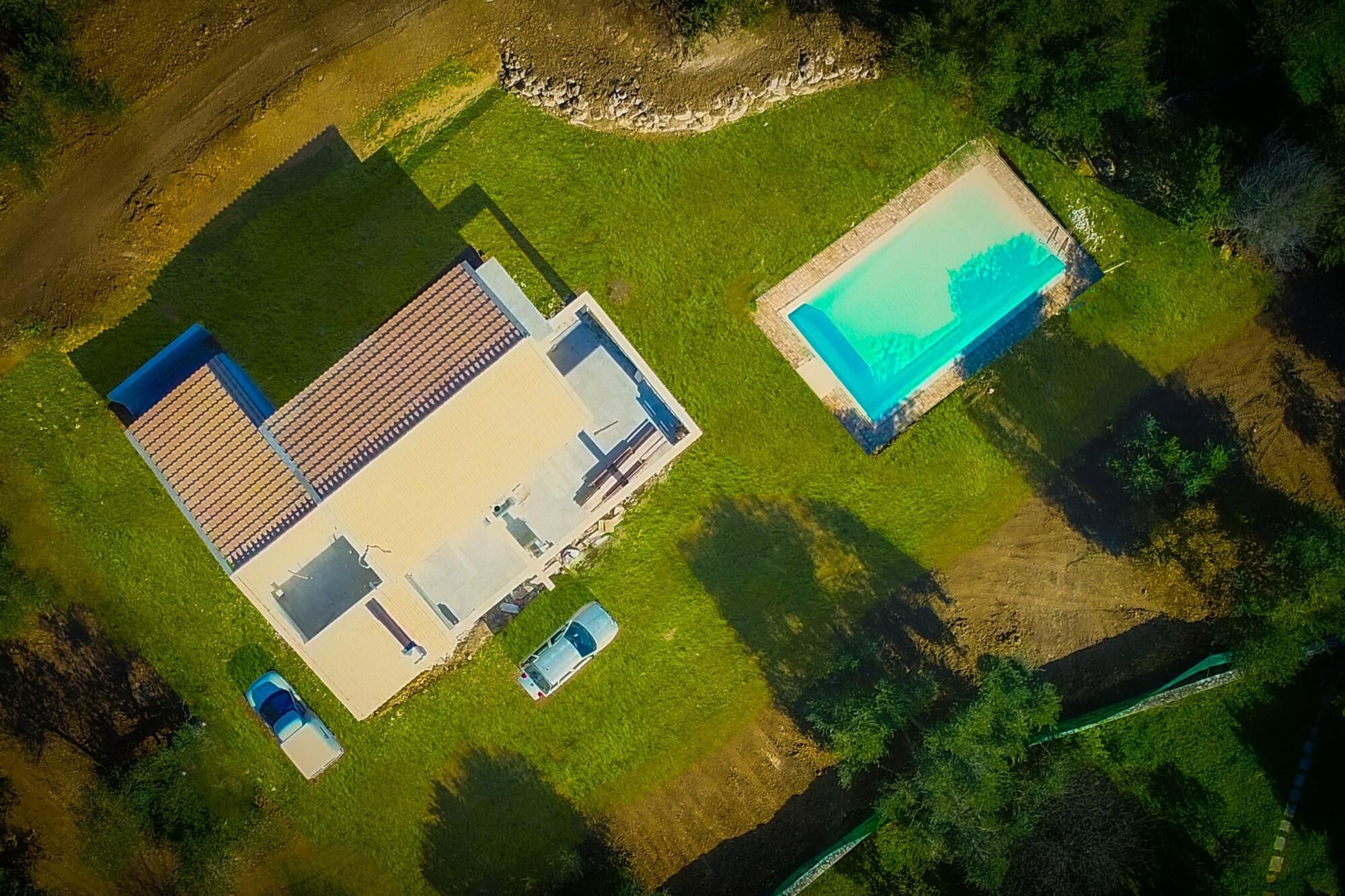 Vista aerea di una proprietà con una grande casa, una piscina e due auto parcheggiate nel vialetto.