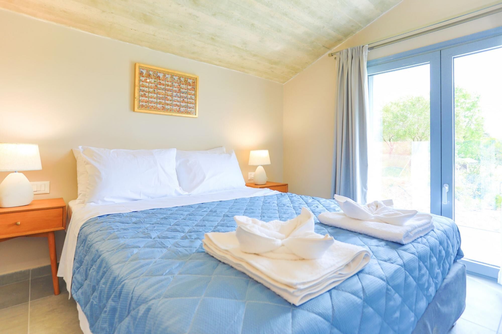 Hotelkamer met een groot bed, twee nachtkastjes, een raam met gordijnen en een kunstwerk aan de muur.