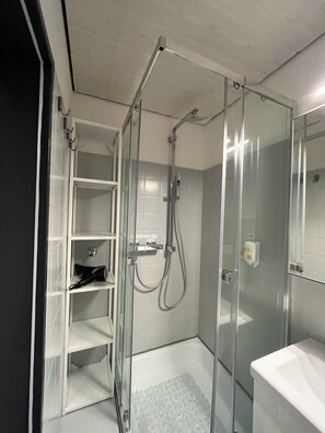 Une salle de bain moderne avec une douche à parois de verre, des murs recouverts de carreaux blancs et un lavabo blanc.