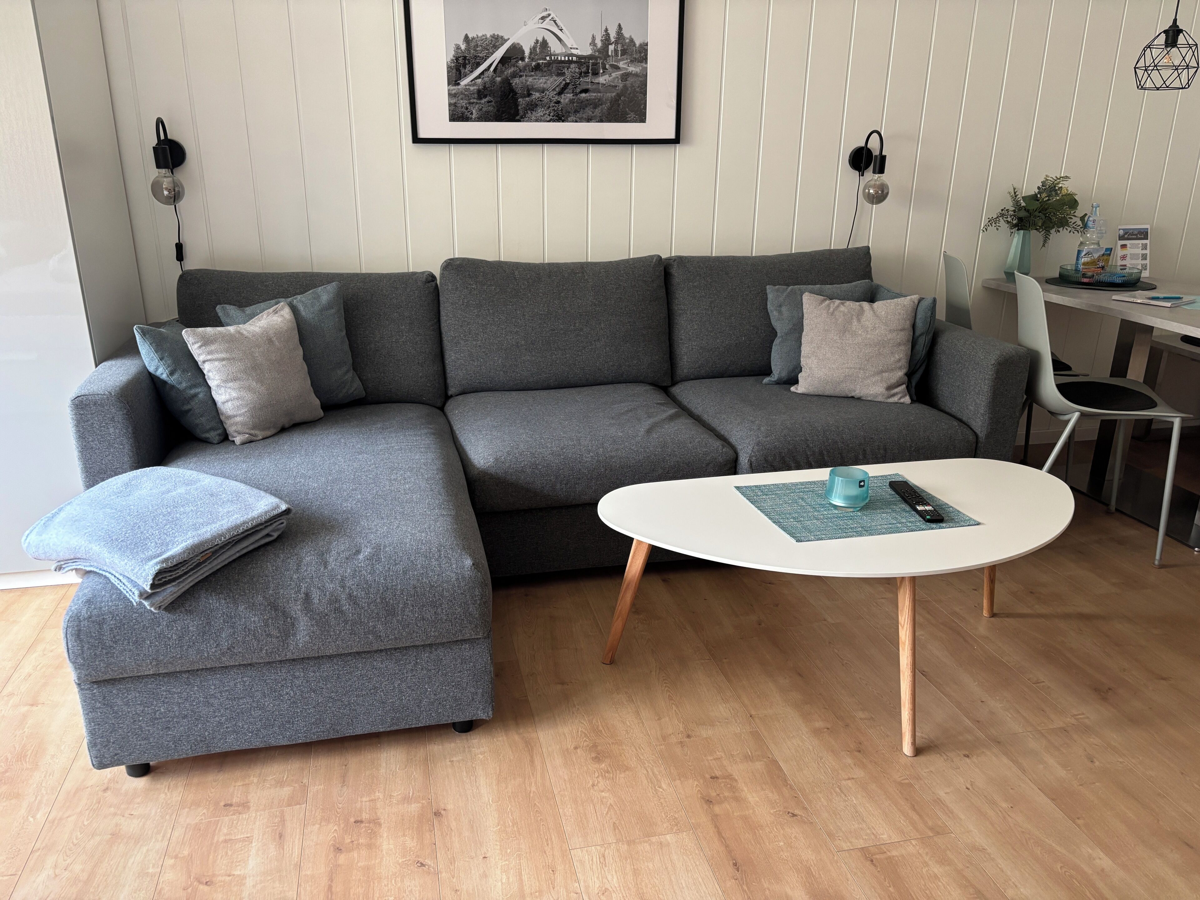 Een grijze modulaire bank met een passende voetenbank, een witte salontafel en een zwart-wit foto in een lijst aan de muur.
