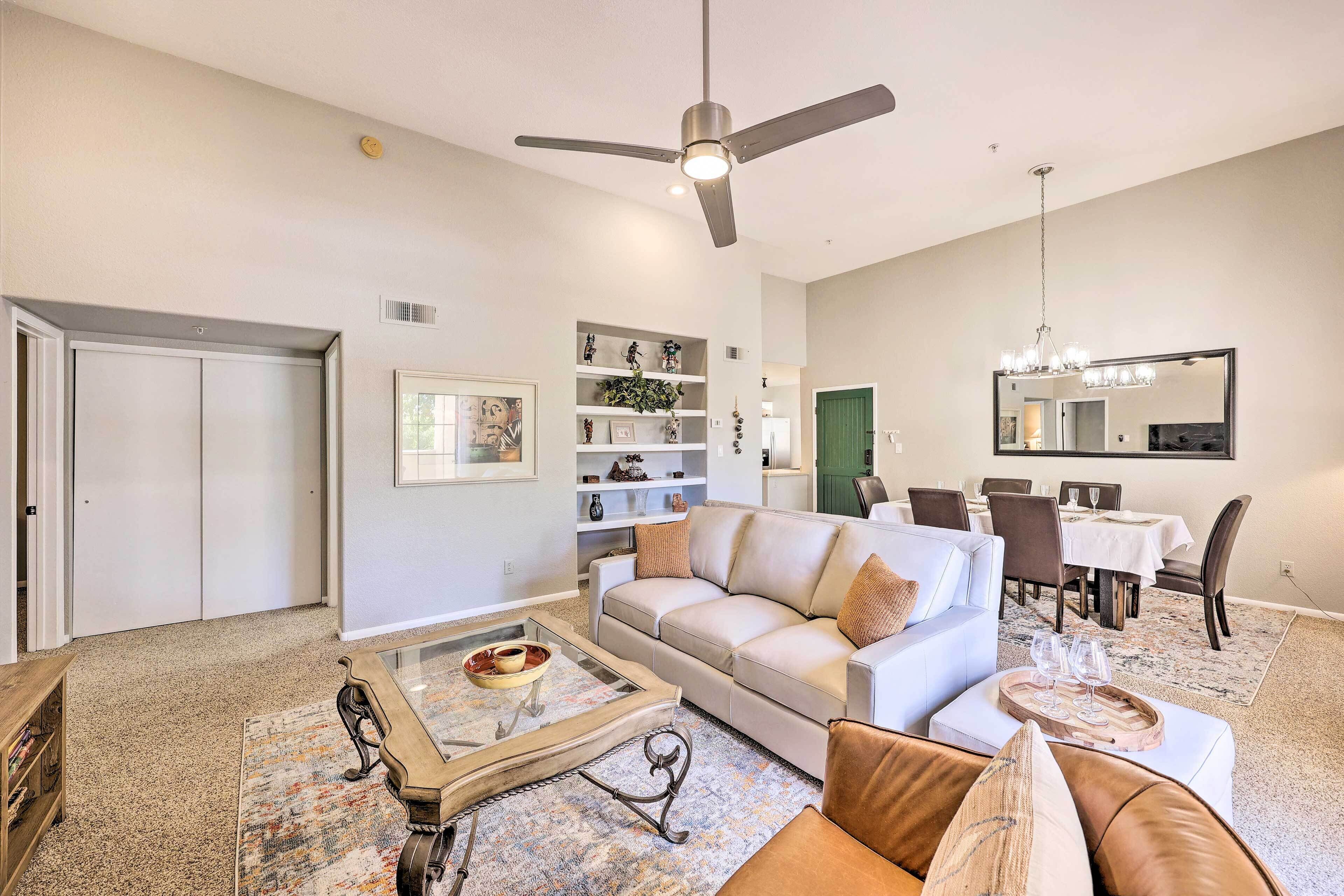 A living room with a white sofa, a coffee table, and a chandelier. There is a dining area with a table and chairs.
