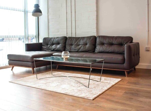 A modern living room with a leather sofa, a glass coffee table, and a patterned rug.