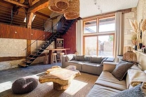 A cozy living room with a wooden staircase, a large window, and a comfortable seating area.