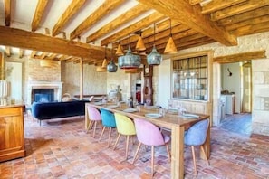 A rustic dining area with exposed wooden beams, a brick floor, and a stone fireplace.