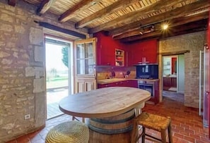 A rustic kitchen with a large wooden table, stone walls, and a stone floor.