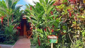 A pathway leading to a building surrounded by lush tropical vegetation. A sign indicates a parking area for the tenorio room. - Jardín entre Montañas (Bijagua)