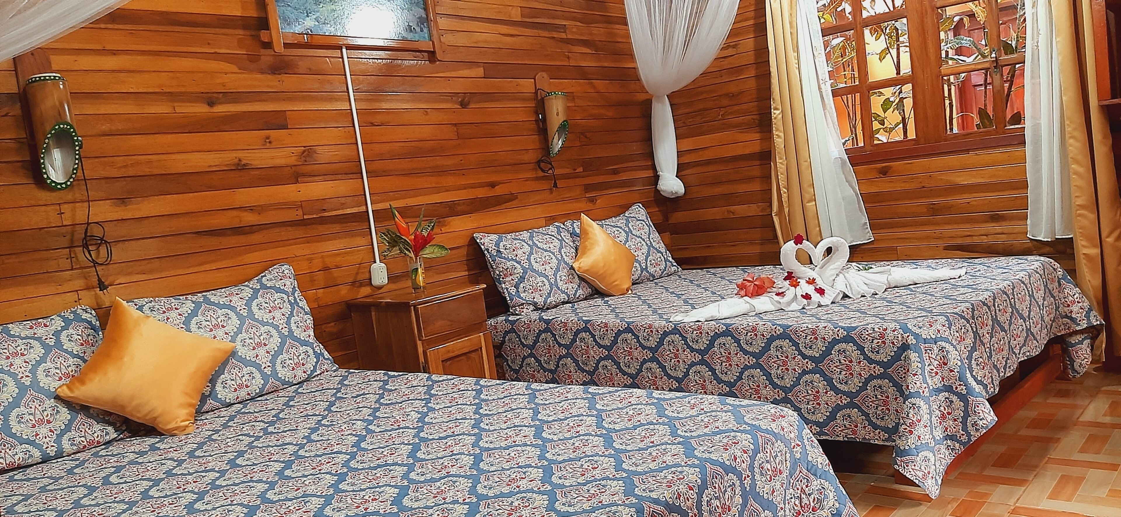 A room with two beds, wooden walls, and a window with curtains.