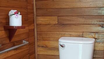 Un baño con pared de madera, un inodoro blanco, un cubo de basura y una repisa con un objeto decorativo.