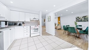 Una cucina moderna con mobili bianchi, forno integrato e forno a microonde. C'è un'area pranzo con un tavolo in vetro e sedie verdi.