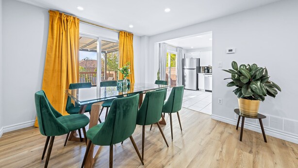 Zona pranzo moderna con tavolo in vetro e sedie verdi, una pianta in vaso e vista sulla cucina e sull'area esterna.