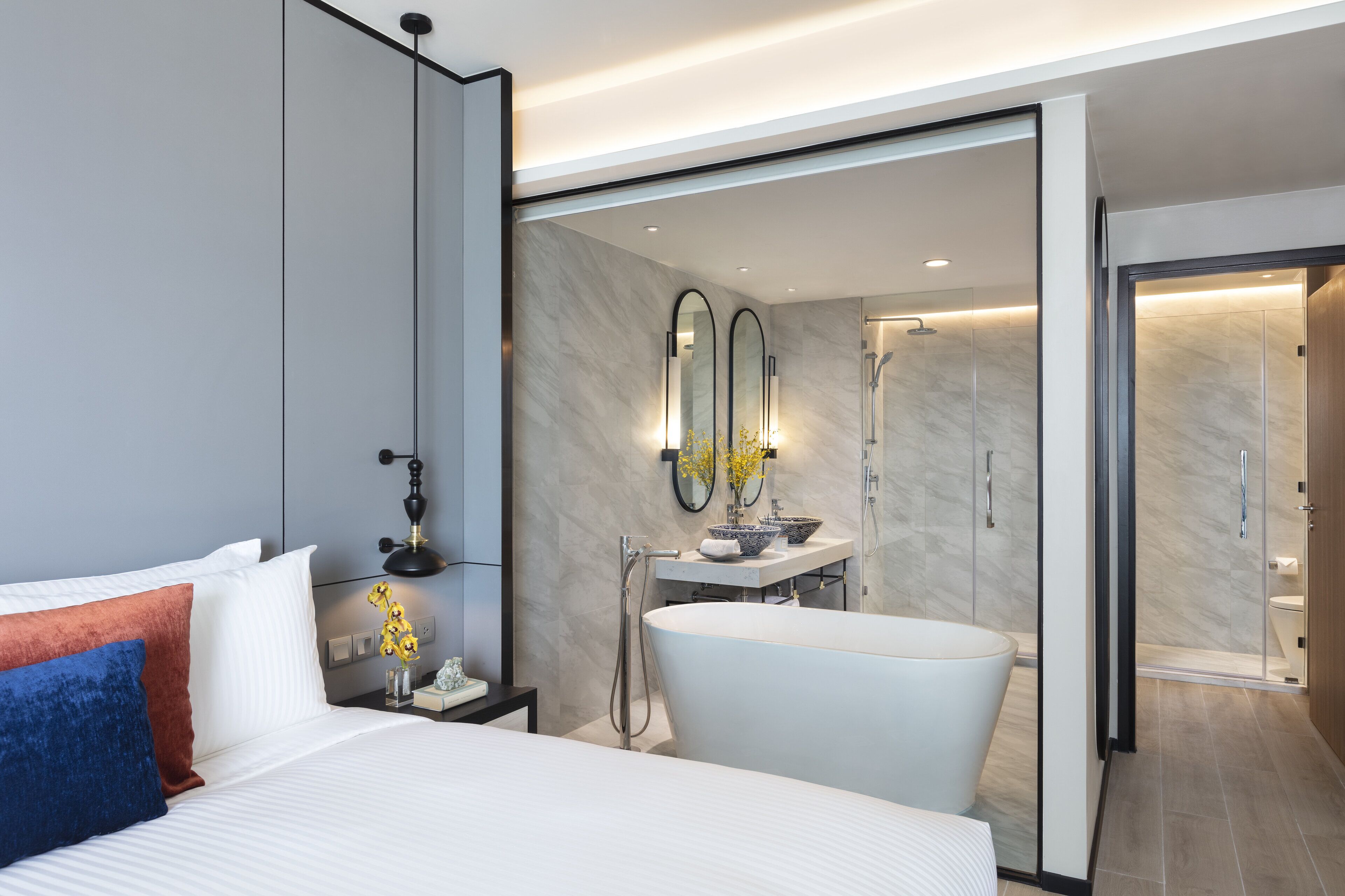 A modern hotel room with a large bed, a bathtub, a vanity with mirrors, and a shower.