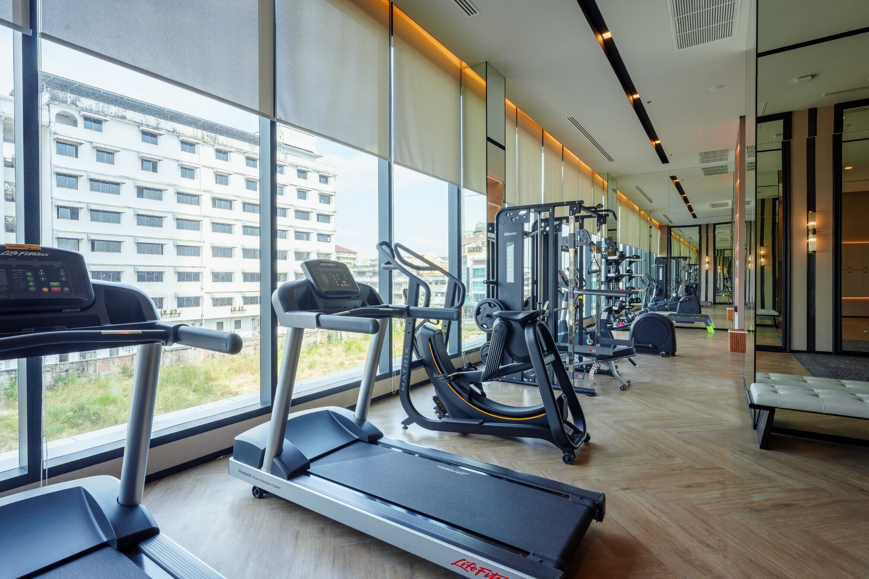 A modern gym with treadmills, weight machines, and a large window offering a city view.