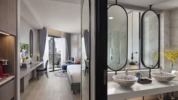 A modern hotel room with a large bed, a sitting area with a sofa and a small table, a bathroom with two large mirrors and a sink with decorative bowls.