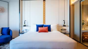 A modern hotel room with a large bed, two bedside tables, a nightstand, a blue armchair, and a large window.