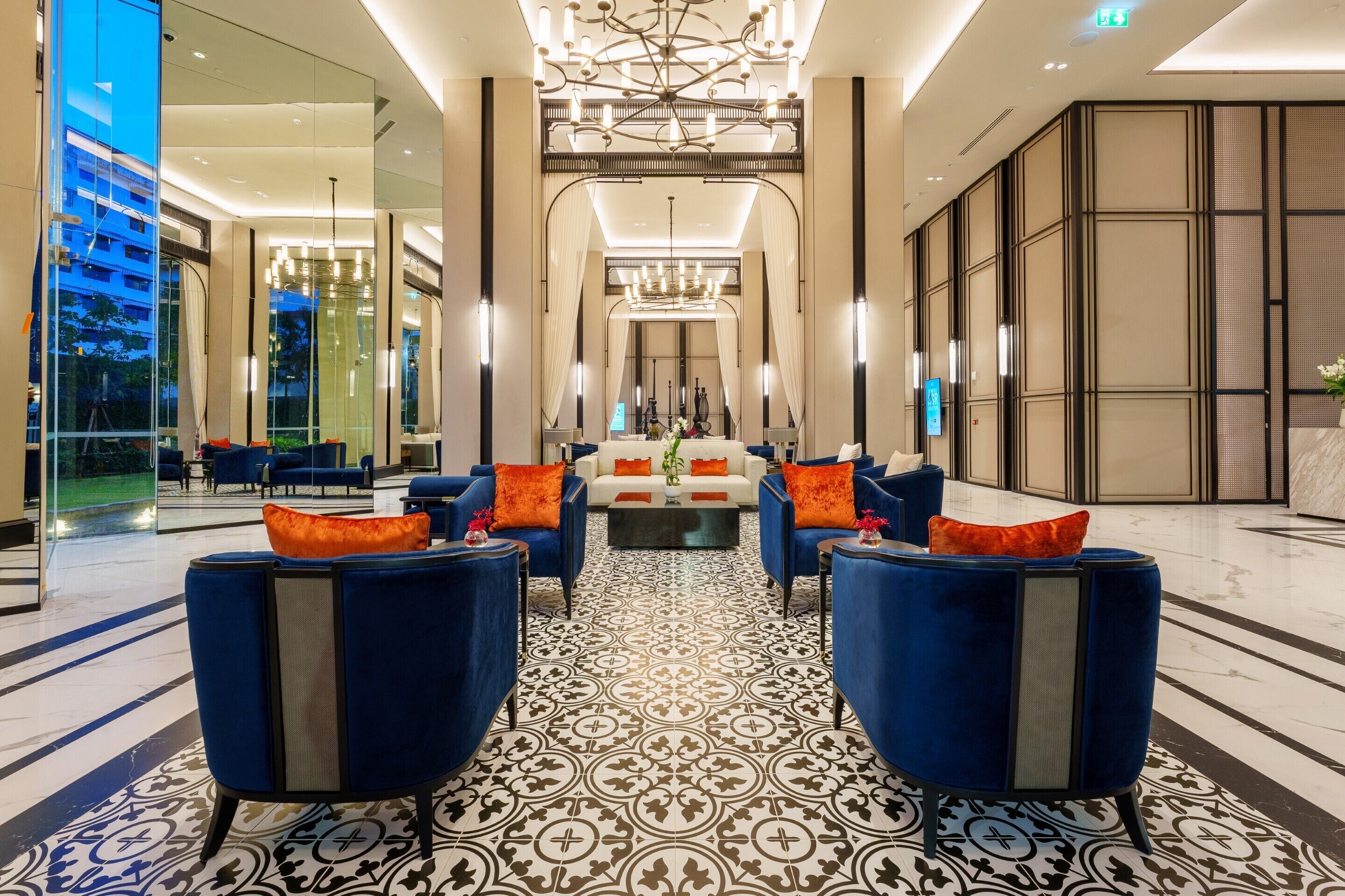 A modern lobby with a patterned floor, blue armchairs with orange cushions, and a central white sofa.