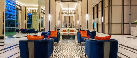 A modern lobby with a patterned floor, blue armchairs with orange cushions, and a central white sofa.