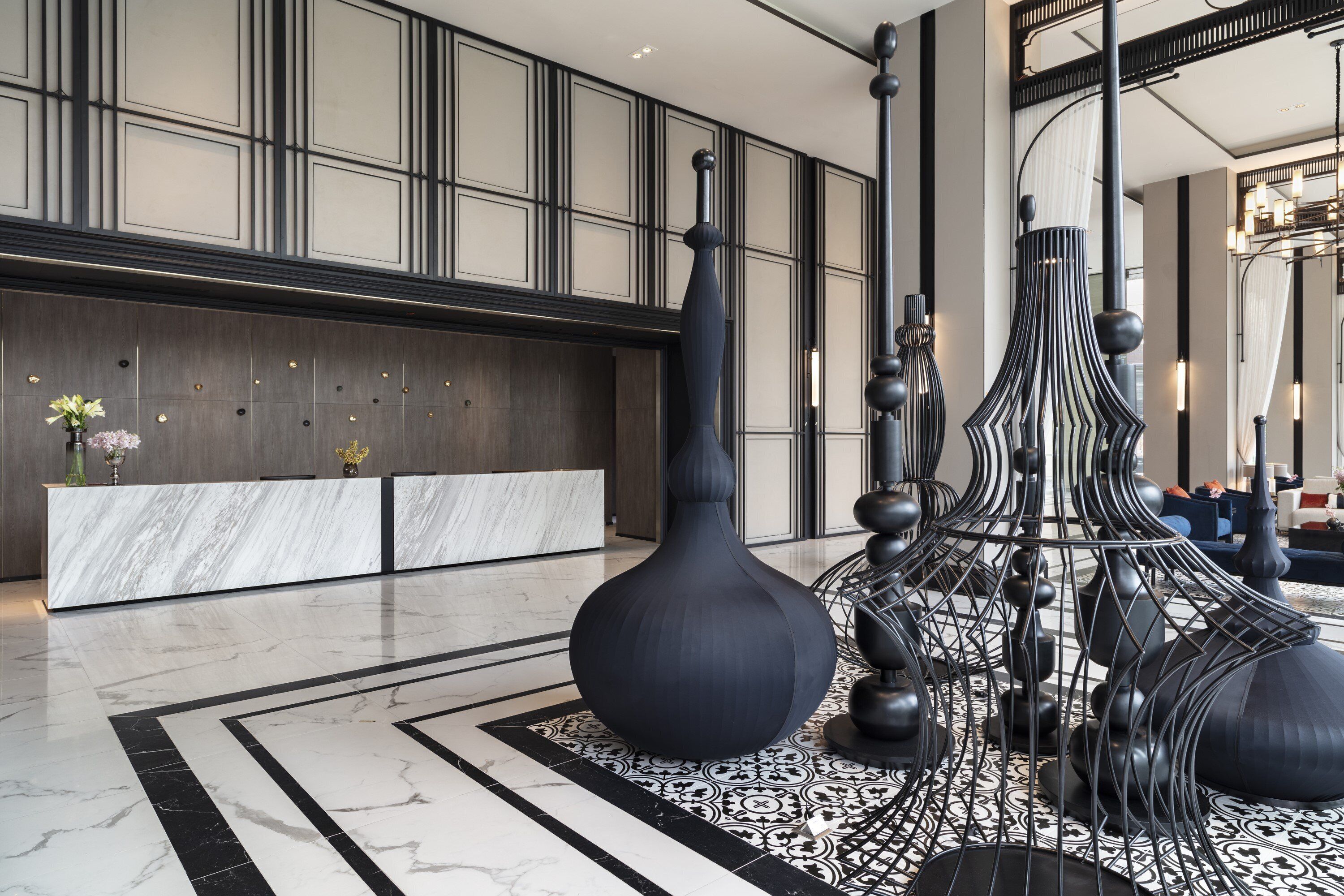 A modern lobby with a marble reception desk, large vases, and a patterned floor.