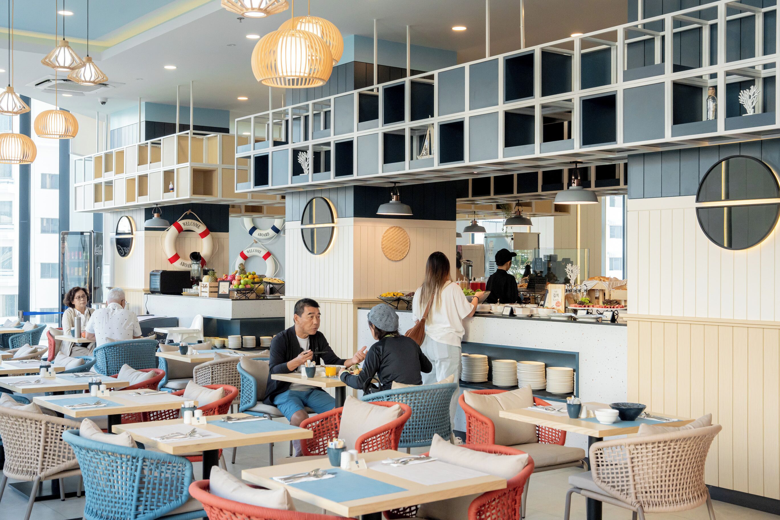 A modern restaurant with wicker furniture, a bar area, and a high ceiling with hanging lights.