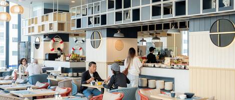 A modern restaurant with wicker furniture, a bar area, and a high ceiling with hanging lights.