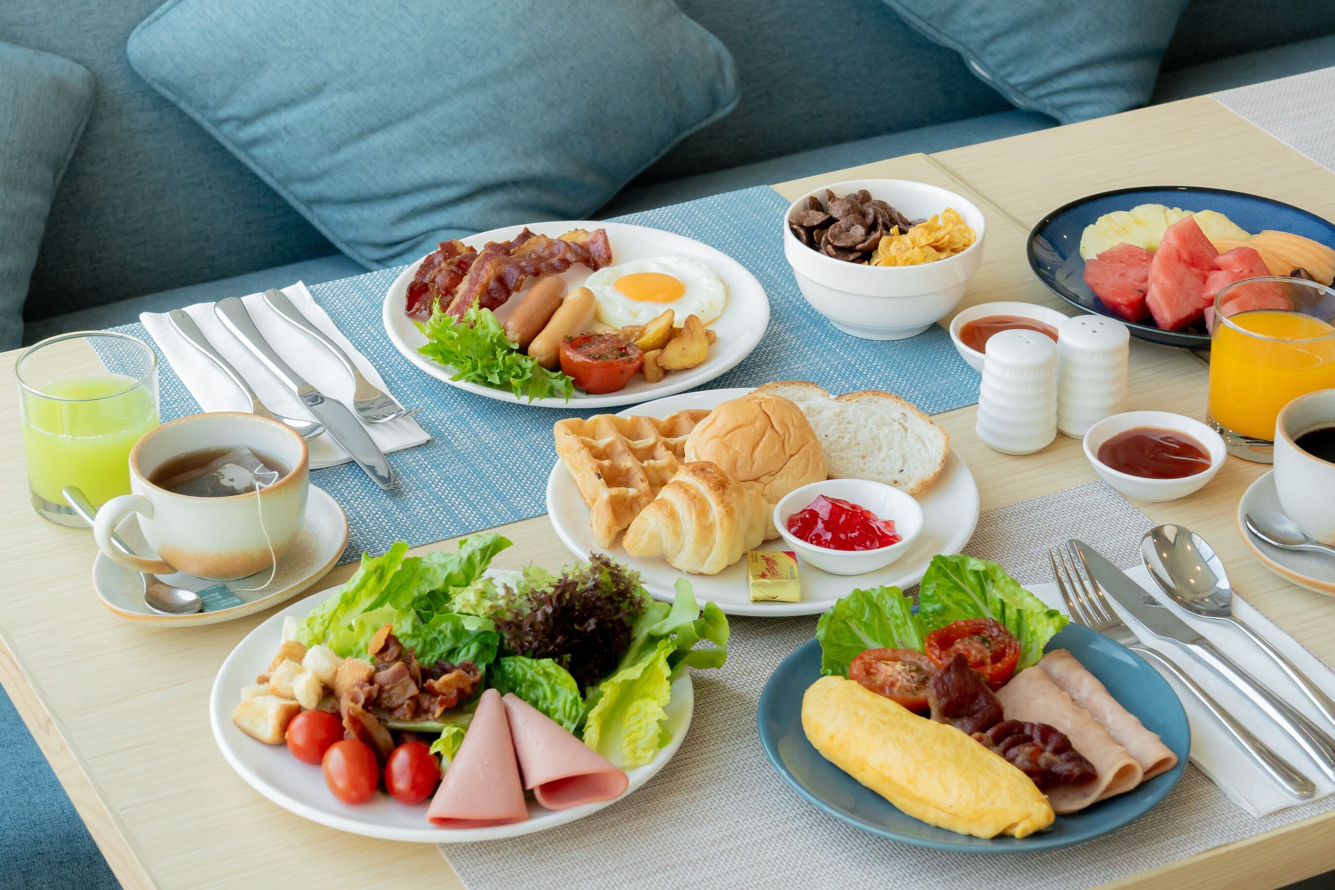 Een ontbijttafel met diverse gerechten, zoals eieren, spek, worstjes, toast en fruit.