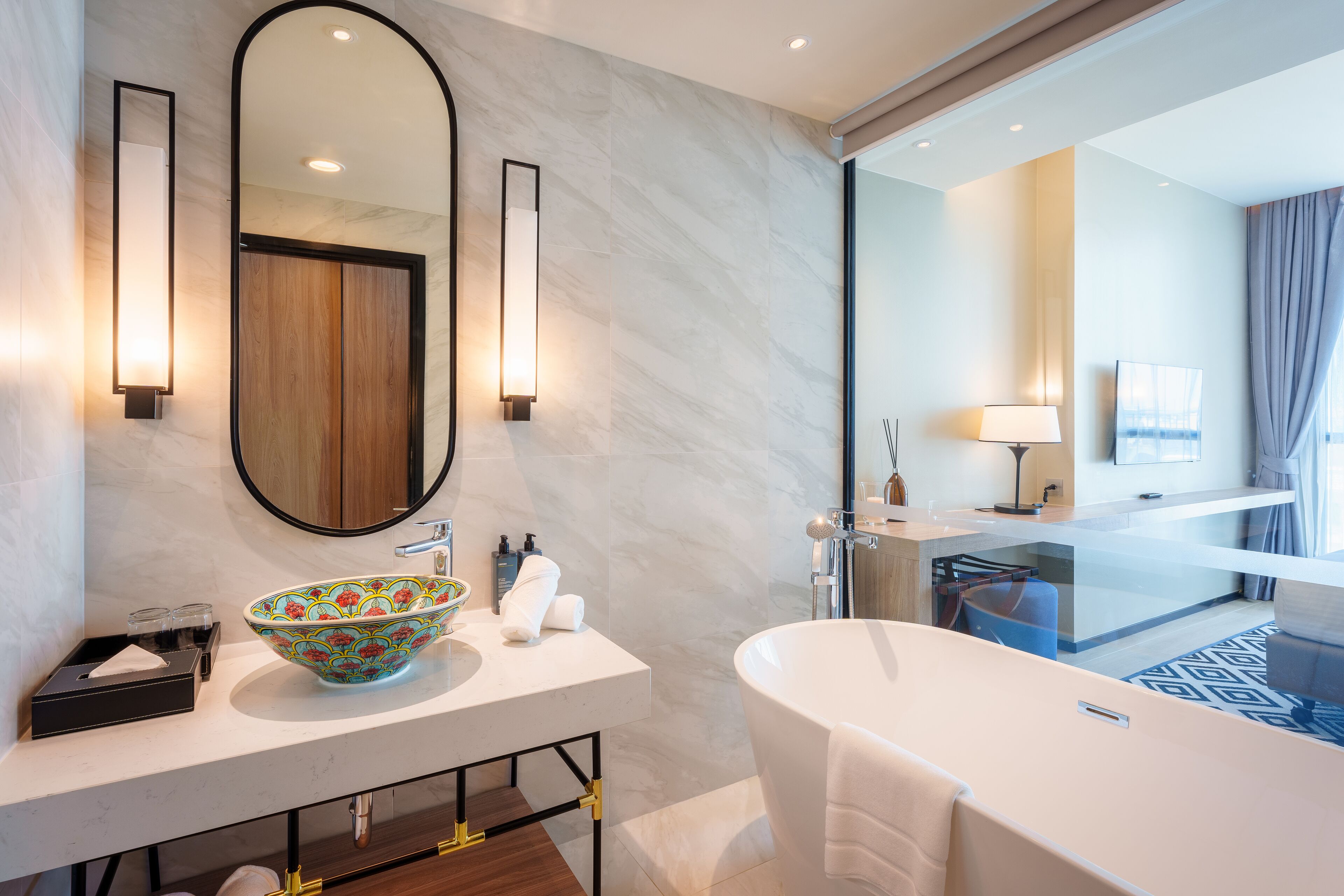 Une salle de bain moderne avec un grand miroir ovale, un lavabo blanc agrémenté d’un récipient décoratif, une baignoire sur pieds et une douche séparée par des parois en verre.
