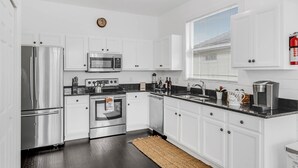 A modern kitchen with white cabinetry, stainless steel appliances, and a black countertop.