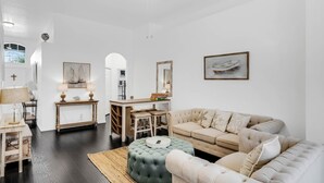 A spacious living room with a large sofa, a round ottoman, a dining area with a table and chairs, and a ceiling fan.