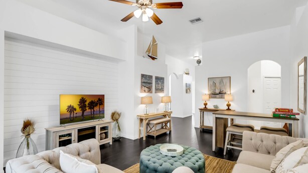 A spacious living room with a large TV, comfortable seating, a ceiling fan, and a dining area with a wooden table and chairs.