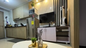 A modern kitchen with wooden cabinets, a stainless steel refrigerator, a microwave, and a flat-screen TV.